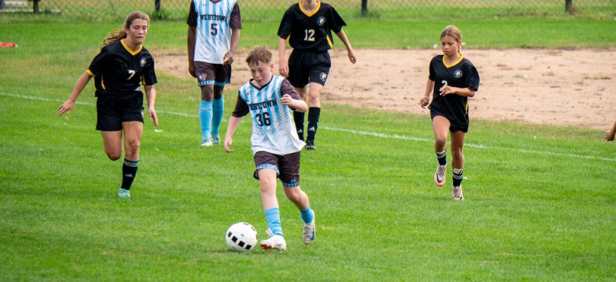 Westtown School middle-school soccer player (#36) dribbling the ball upfield while opposing defenders in black jerseys chase during a competitive youth match on a grass field.