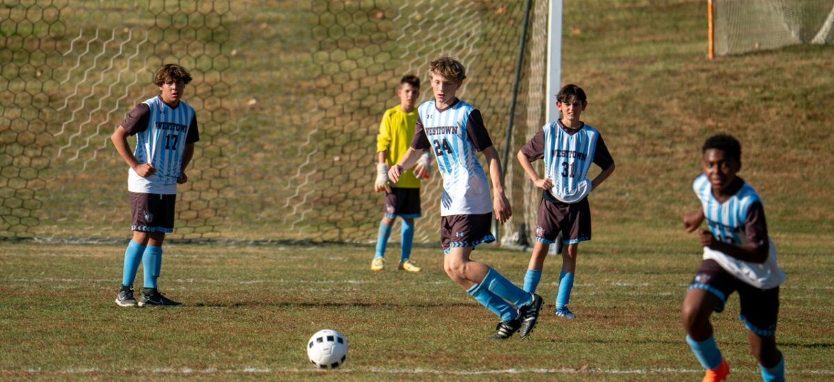 Middle-school boys in Westtown jerseys stand by their goal while a teammate advances the ball upfield.