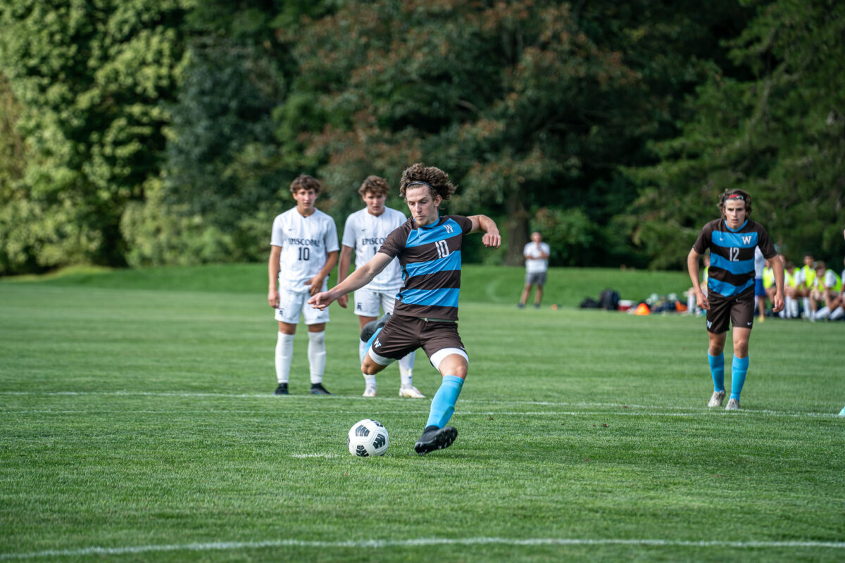 Boys Varsity Soccer team member kicking a ball during a game