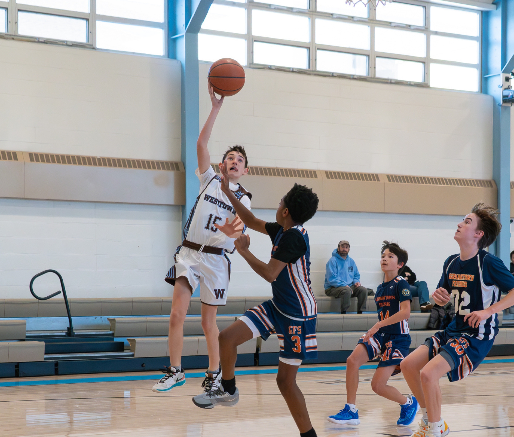 Westtown School middle-school player in a white uniform leaping for a layup while defenders contest the shot during a winter season game in the school gym.