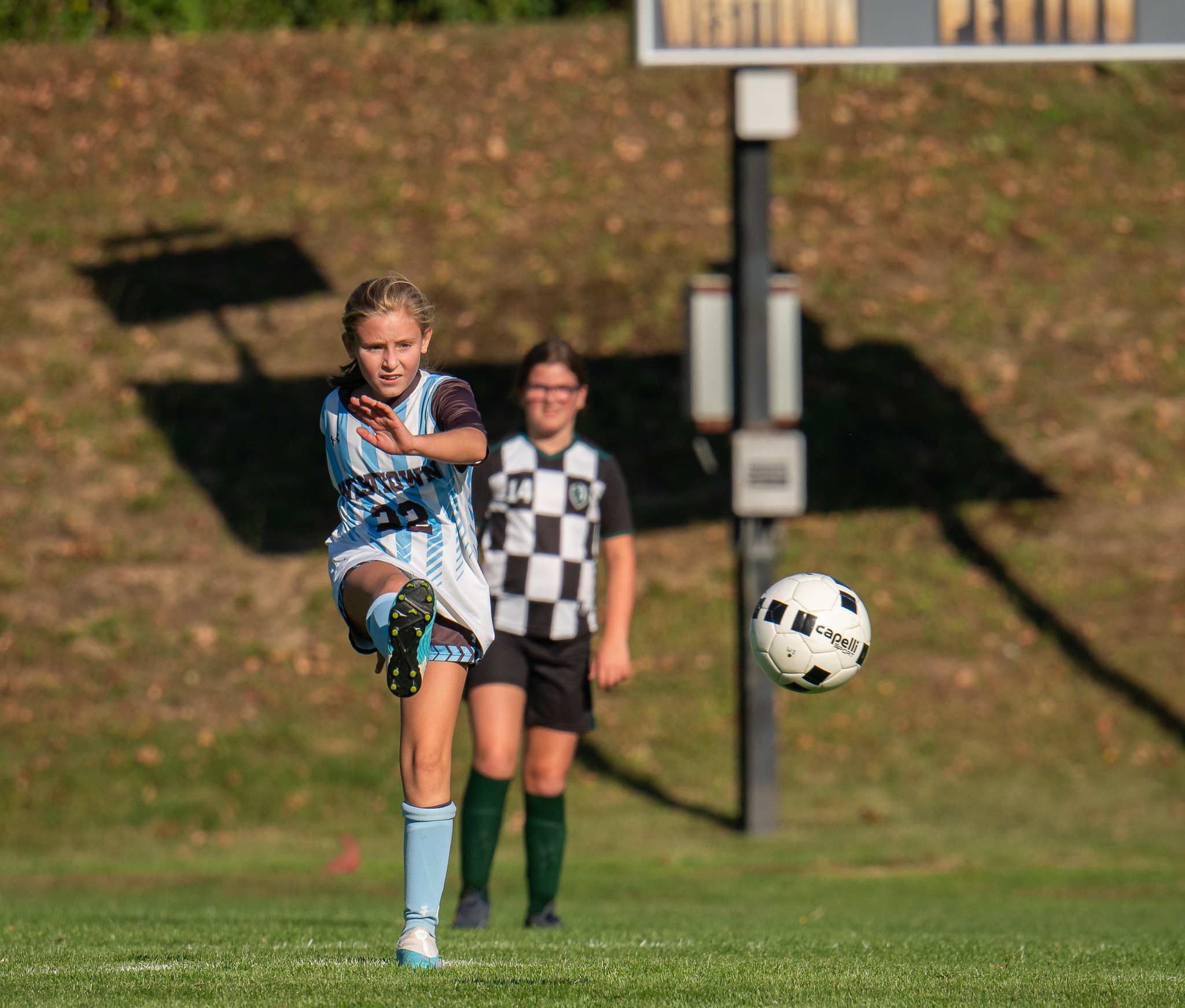 Westtown School middle-school girls soccer player in light-blue kit powering a long kick downfield during an autumn match.